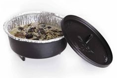 an aluminum foil container filled with food on top of a white table next to a black pot