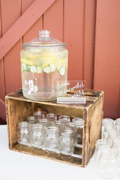 a wooden crate filled with lots of glasses and a jar full of lemonade sitting on top of a table