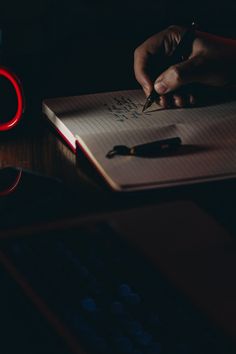 a person writing on a notebook with a red light in the dark next to them