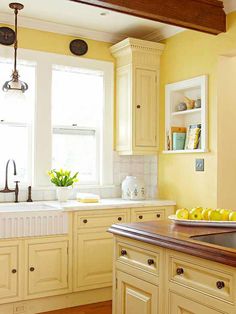 a kitchen with yellow painted cabinets and wood floors in the center is an island that has fruit on it