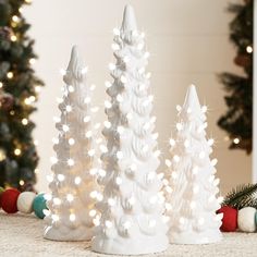 three white christmas trees are sitting on the floor next to a tree with lights in it