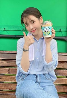 a woman sitting on a bench holding a jar of food and giving the peace sign