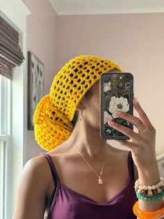 a woman wearing a yellow crochet hat taking a selfie with her cell phone