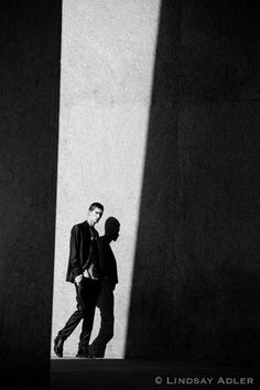 two men standing next to each other in front of a wall with their shadows on it