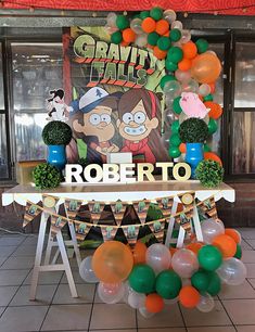 a table with balloons and decorations on it in front of a giant balloon banner that reads, gravity falls robertto