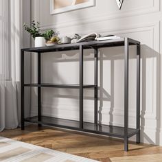 a black console table with books and plants on it in front of a white wall