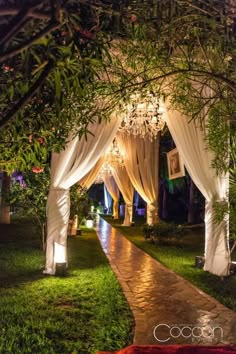 an outdoor wedding venue with white drapes and chandeliers on the ceiling, surrounded by greenery