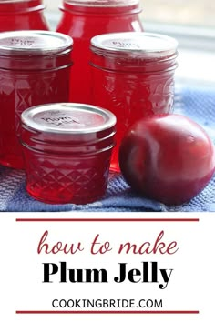 four jars filled with plum jelly sitting on top of a blue towel next to an apple