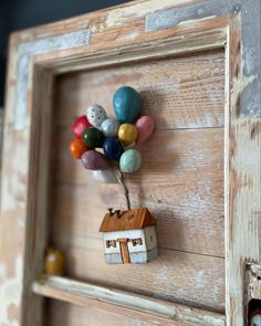 a small house with balloons attached to the front of it, mounted on a wooden frame