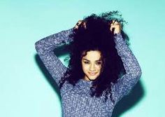 a woman with curly hair is posing for a photo in front of a blue background