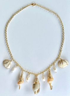 The Seashell and Freshwater Pearl Necklace  is a dazzling piece that captures the serene beauty of summer's coastal magic. Perfect for adding a touch of seaside elegance to any outfit, this necklace features a stunning combination of seashells with gold accents and freshwater pearl charms. The centerpiece of this captivating necklace is a collection of seashells delicately accented with gold, each one evoking the timeless allure of the ocean. These seashells are accompanied by lustrous freshwater pearls, creating a harmonious blend of textures and elegance. Strung on a delicate gold chain, the Ocean Jewel Charm Necklace radiates a sense of graceful summer elegance, making it an exquisite accessory for any occasion. Whether you're enjoying a day at the beach, attending a casual summer outin Luxury Gold Shell Necklace With Pearl Charm, Elegant Starfish Charm Jewelry For Vacation, Ocean-inspired Jewelry With Lobster Clasp For Vacation, Vacation Pearl Charm Strand Necklace, Ocean-inspired Jewelry For Vacation With Lobster Clasp, Vacation Strand Necklace With Pearl Charm, Gold Shell Necklace With Starfish Charm On Strand, Elegant Beach Necklace With Lobster Clasp, Summer Beach Necklaces With Pearl Charm