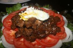 a plate topped with meat and tomatoes on top of lettuce covered in sauce