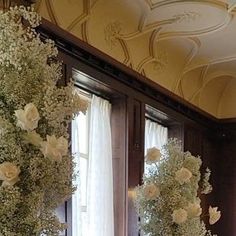 two vases filled with white flowers sitting on top of a table next to windows