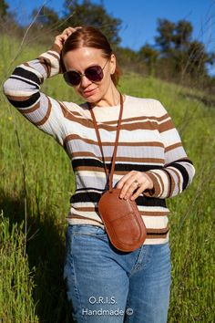 a woman standing in the grass with her hand on her hip wearing sunglasses and a brown leather bag