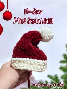 a hand holding a knitted santa hat in front of a christmas ornament