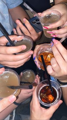 many people are holding their hands together with drinks in small bowls and spoons on the table