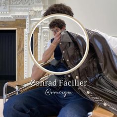 a man sitting on top of a wooden chair in front of a fireplace wearing a leather jacket