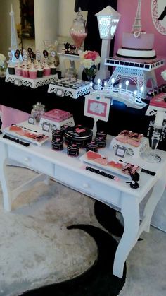 a white table topped with cakes and desserts next to a black cat rug in front of a pink wall