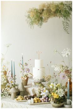 a white cake sitting on top of a table next to flowers and candles in vases