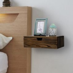 a wooden shelf on the side of a bed with two pictures and a framed photo