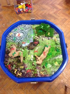 a blue bowl filled with lots of different types of toy animals and plants on top of a wooden floor