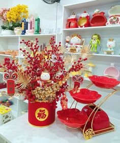 a red vase filled with flowers on top of a white table next to other items