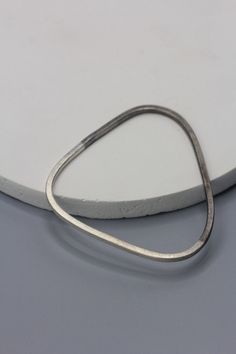 The handmade silver bangle is made of square profile 2.3 mm thick silver wire with etched surface that gives it a more artisanal feel. The peculiarity is in the shape that is  triangular, but with rounded angles so it's comfortable to wear.  We coated half of the bangle in dark grey Rhodium finish.  All our items are handmade in 958 silver in our workshop in the Northern Thailand, by skilled Thai Karen hill tribe silversmiths.  We ship the items from our main office in Bangkok in its original pa Handmade Metal Bangle In Minimalist Style, Handmade Minimalist Metal Bangle, Minimalist Handmade Metal Bangle, Minimalist Silver Stackable Bangle, Northern Thailand, Silver Bangle, Triangle Shape, Style Expert, Silver Bangles