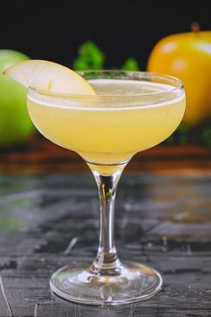 a glass filled with a yellow liquid next to some green peppers and an orange on the table