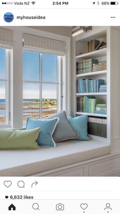 a window seat with bookshelves and pillows on it in front of two windows