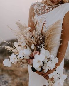 a woman in a white dress holding a bouquet of flowers and grass with her hands