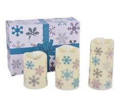 three candles with snowflakes on them next to a gift box