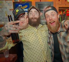 two men are posing for the camera with their hands in the air and one is holding a beer