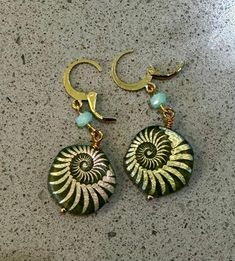 pair of earrings with green and gold designs on the front, sitting on top of a counter