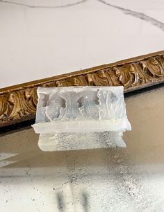 a piece of ice sitting on top of a table next to a mirror with an ornate gold frame