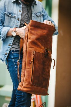 a man holding a brown leather bag in his hands and looking down at the ground