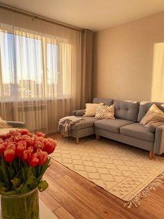 a living room filled with furniture and flowers in a vase on top of a wooden floor