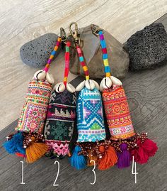 four colorful bags with tassels hanging from them on a wooden floor next to rocks