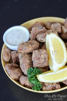 a yellow bowl filled with meatballs and lemon wedges next to a dipping sauce