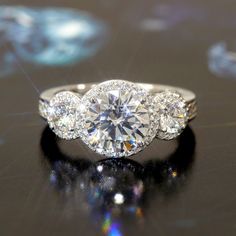 three stone diamond ring sitting on top of a black surface with light shining in the background