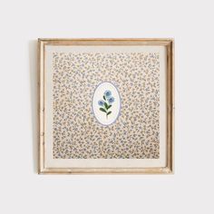 a painting with blue flowers on it in a wooden frame hanging on a white wall