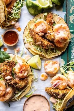 three shrimp tacos with lime wedges and dipping sauce on the side next to them