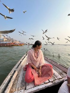 a woman sitting in a boat with seagulls flying over her and on the water