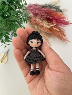 a hand holding a tiny doll next to a plant