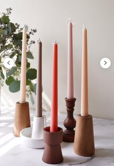 five candles are lined up in different shapes and sizes on a white table with greenery