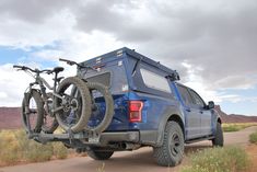 a blue truck with two bikes on the back of it's rack in the desert