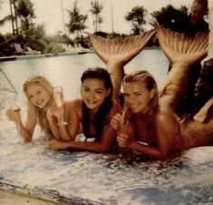 three beautiful young women laying on top of a swimming pool next to eachother