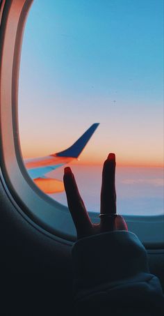 the view from an airplane window at sunset with someone's hand on the wing