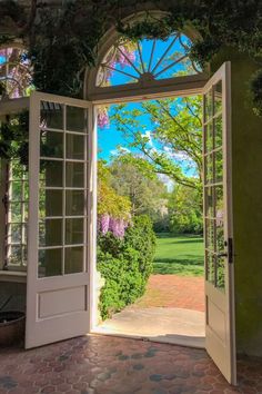 an open door leading into a lush green park with trees and flowers on either side