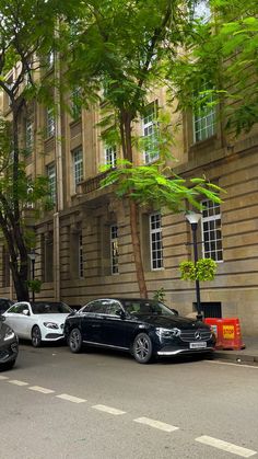 several cars parked in front of a building on a city street with tall buildings behind them