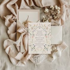 wedding stationery with flowers and ribbons on top of a bed sheet, next to a bouquet of flowers